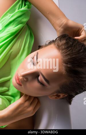 Una giovane donna si rilassa nella vasca da bagno indossando un indumento verde brillante Foto Stock