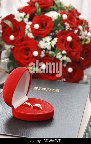 Rose rosse e fedi nuziali sulla bibbia Foto Stock