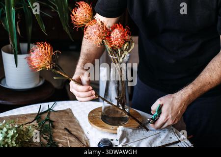 Primo piano di mani impegnate in attività di composizione floreale per promuovere il benessere mentale e la presenza consapevole attraverso l'interazione botanica creativa Foto Stock