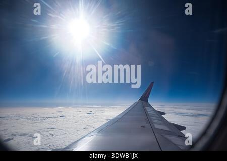 Basilea, Svizzera, 10 febbraio 2025. Ala dell'aeroplano visibile dalla finestra con un sole luminoso che splende sopra le nuvole in un cielo blu chiaro durante il volo sopra t Foto Stock
