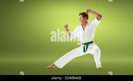 Lottatore di karate in gi bianchi che esegue una forte posizione difensiva con cintura verde. Foto Stock