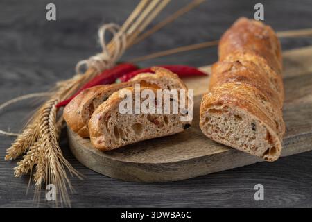 Baguette di frumento di segale con crusca e peperoni su un asse di legno. Foto Stock