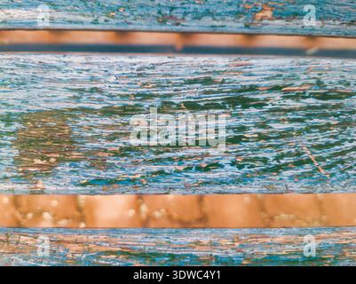 Primo piano ad alta risoluzione di un banco o di una recinzione in legno intemprato. L'immagine mostra strati di vernice blu e verde sbiancati su legno naturale, perfetto Foto Stock