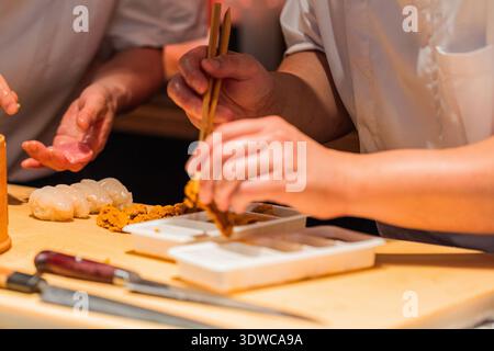 Lo chef esperto prepara il sushi utilizzando ingredienti freschi, mostrando precisione e maestria in un vivace ambiente di cucina. Foto Stock