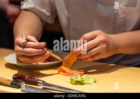 Lo chef esperto prepara il sushi con ingredienti freschi, utilizzando strumenti di precisione, dimostrando l'esperienza culinaria e l'attenzione ai dettagli. Foto Stock