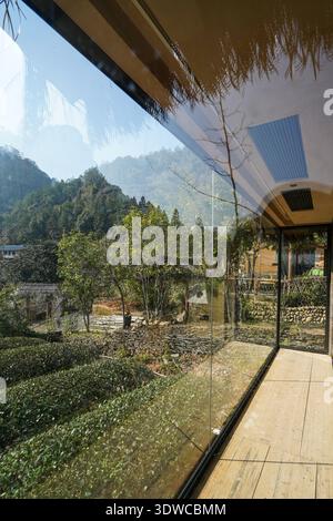 Titolo: Vista della Mountain Peak Valley attraverso la parete di vetro con soffitto Thatch del moderno Rural Lodge Foto Stock