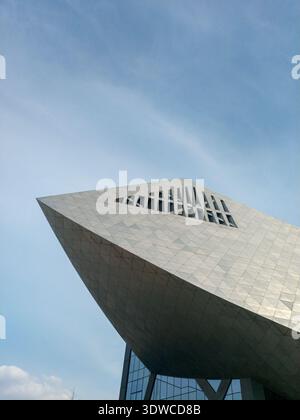Una prospettiva ad angolo basso di una struttura architettonica contemporanea che mostra angoli drammatici e rivestimenti in pietra sotto un cielo azzurro. Foto Stock