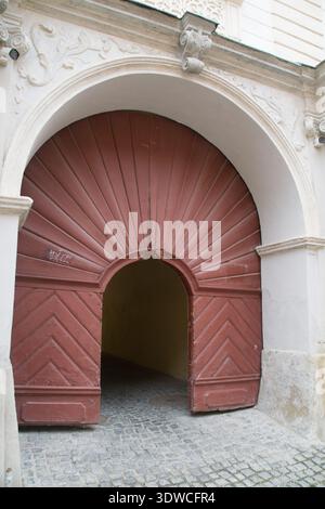 Una grande porta in legno dal design unico sorge all'entrata di un vicolo a Brasov Romania. I dintorni mostrano una vecchia architettura. Foto Stock
