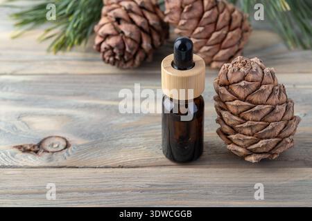 Bottiglia di olio essenziale di cedro, coni di pino e rami di ago verdi su un tavolo di legno. Prodotti a base di noci di cedro per il relax e il massaggio nel centro benessere. Foto Stock