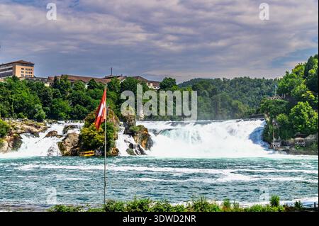 Un colpo largo cattura la potente cascata Rheinfall in Svizzera. L'acqua a cascata crea uno spruzzo nebbioso, in contrasto con il lussureggiante vegetale Foto Stock