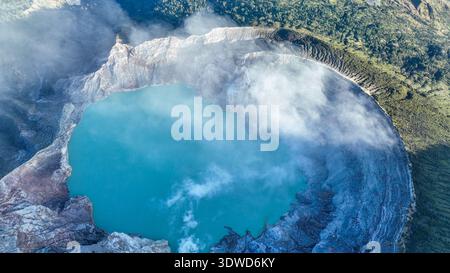 Vista dall'alto del lago turchese con acque solforose, circondato da una scogliera rocciosa presso il vulcano Kawah Ijen a Giava Est, Indonesia. Foto Stock