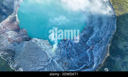 Vista dall'alto del lago turchese con acque solforose, circondato da una scogliera rocciosa presso il vulcano Kawah Ijen a Giava Est, Indonesia. Foto Stock