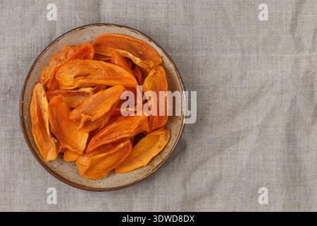 Fette di cachi essiccati maturi in un piatto sul tavolo. Uno spuntino sano. Un regalo. Messa a fuoco selettiva, vista dall'alto Foto Stock
