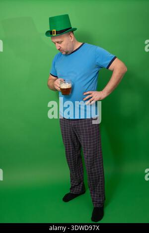 Uomo che indossa un cappello verde di leprechaun e tiene una tazza di birra spumanta su sfondo verde. Festa di San Patrizio con celebrazione irlandese e tradizione dei pub. fotografia Foto Stock