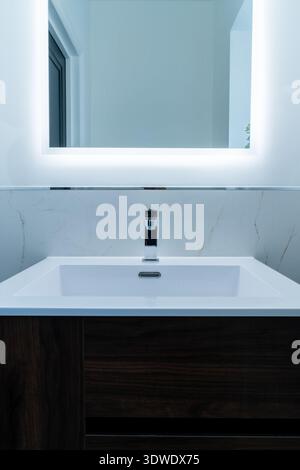 Un moderno lavandino da bagno con un elegante rubinetto e uno specchio illuminato esaltano l'elegante design di una casa londinese. Lo stile elegante trasuda Foto Stock