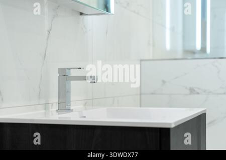 Bagno dal design elegante con elegante rubinetto cromato e pareti in marmo bianco. L'estetica moderna include un armadio in legno scuro che offre un lusso Foto Stock