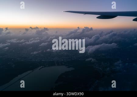 Una splendida vista aerea di Cancun all'alba, catturata dalla finestra di un aereo. Le luci della città si fondono con la bellezza naturale delle nuvole e lontane Foto Stock