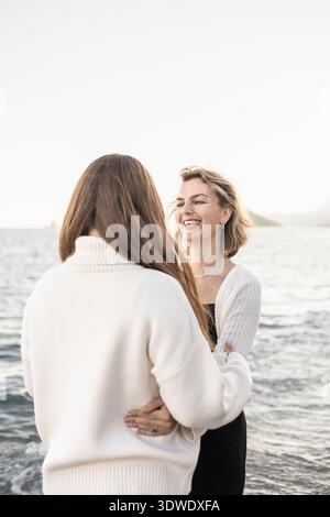 Un momento di gioia catturato tra una madre e una figlia che si godono il loro tempo in spiaggia. Lo sfondo sereno e il loro abbigliamento casual mettono in risalto il W Foto Stock