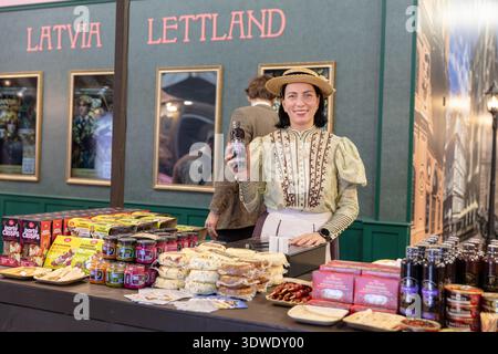 BERLINO, GERMANIA, 16 gennaio 2026: La foto di Una donna in abito tradizionale lettone si trova in uno stand che promuove prodotti alimentari e bevande locali presso il Foto Stock