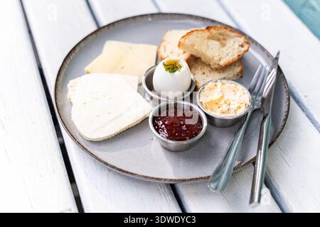 Una deliziosa colazione a base di fette di formaggio fresco, uova sode, pane croccante, burro cremoso e un lato di marmellata. Perfetto per iniziare a. Foto Stock