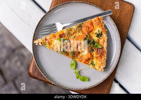 Una deliziosa fetta di crostata con salmone affumicato salato, formaggio cremoso ed erbe fresche, servita su un piatto di ceramica con una forchetta. Perfetto per una delizia Foto Stock