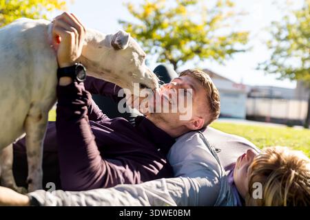 I fratelli si godono un momento di gioia all'aperto, sdraiati sull'erba sotto il sole, giocando con il loro cane amico, creando una scena di amicizia e. Foto Stock