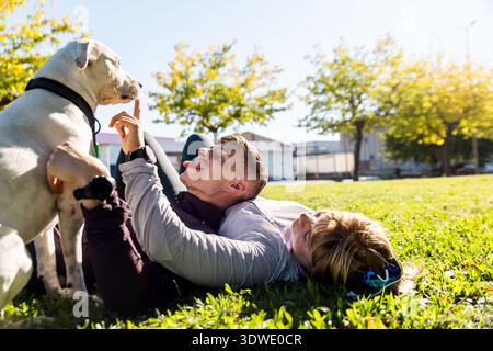 I fratelli si godono un momento di gioia all'aperto, sdraiati sull'erba sotto il sole, giocando con il loro cane amico, creando una scena di amicizia e. Foto Stock