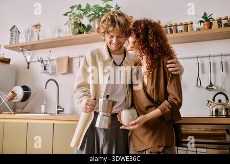 La giovane coppia ride e si connette mentre prepara il caffè nella loro elegante cucina. Foto Stock