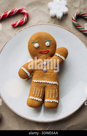 Un delizioso biscotto di pan di zenzero decorato con glassa è collocato su un piatto bianco. Circondato da canne di caramelle e un fiocco di neve, cattura l'essenc Foto Stock