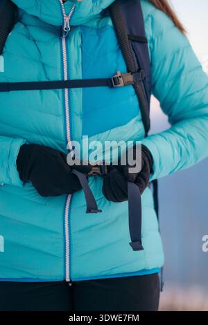 Uno scatto ravvicinato di una donna che indossa le cinghie dello zaino mentre esplora il paesaggio invernale innevato a Lofoten, Norvegia. Vestito caldo con una giacca blu Foto Stock