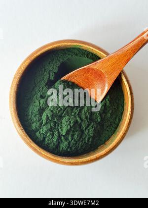 Polvere di spirulina organica in recipiente di legno con cucchiaio su sfondo bianco. Alghe superfood ricche di sostanze nutritive, perfette per disintossicazione, frullati e benessere. Foto Stock