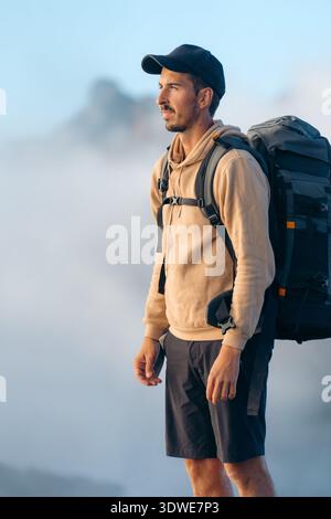 Un avventuriero solitario si ferma durante un trekking mattutino a Madeira, circondato da montagne nebbiose. Indossato con cappuccio e cappuccio, incarna lo spirito di e. Foto Stock