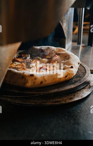 Una pizza appena sfornata emerge dal forno in una tradizionale pizzeria napoletana, che mostra la sua crosta perfettamente croccante e condimenti salati, incarnando Foto Stock