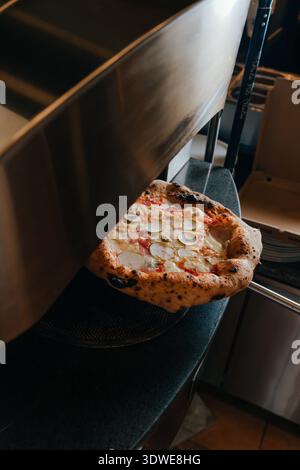 Una pizza napoletana appena sfornata emerge da un tradizionale forno pizzeria. La crosta fatta a mano e le guarnizioni gorgoglianti mostrano l'autentico culinario italiano Foto Stock
