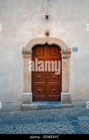 Una porta in legno splendidamente realizzata adagiata in un arco di pietra su una strada pittoresca a Cefalù, in Sicilia. Cattura il fascino e l'eleganza rustica della cucina italiana Foto Stock