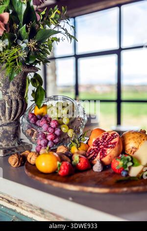 Un vivace spettacolo di frutta assortita come fragole, mirtilli, uva e melograni, abbinato a noci e formaggi su un tavolo rustico. Foto Stock