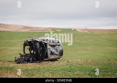 Un veicolo rovesciato giace su un campo erboso dopo un incidente stradale, evidenziando le conseguenze di una grave collisione stradale e sottolineando la strada Foto Stock