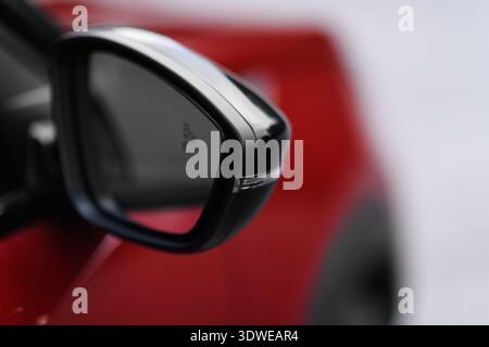Una fotografia dettagliata in primo piano che si concentra sullo specchio laterale di un elegante veicolo rosso moderno. Foto Stock