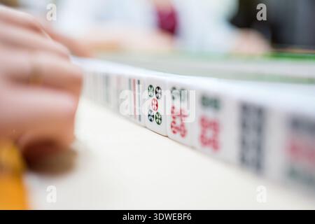 Un'immagine ravvicinata cattura l'atmosfera coinvolgente di un gioco del Mahjong, mostrando mani e tessere dei giocatori. Questo riflette le tradizioni culturali e la promozione Foto Stock