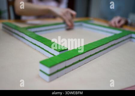 Primo piano di vivaci piastrelle del Mahjong su un tavolo durante una coinvolgente sessione di gioco. Le mani dei giocatori muovono abilmente i pezzi, riflettendo strategia e cultura Foto Stock