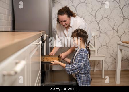 Una madre e una figlia condividono un momento di gioia mentre preparano i biscotti nella loro accogliente cucina. La madre guida sua figlia, promuovendo un atmo amorevole di famiglia Foto Stock