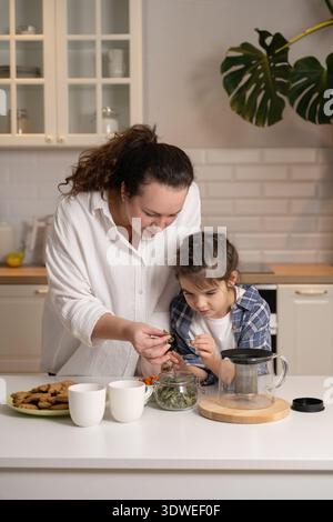 Una madre e una figlia condividono un momento speciale in cucina, preparando il tè alle erbe insieme. Sono concentrati e sorridenti, evidenziando il calore e. Foto Stock