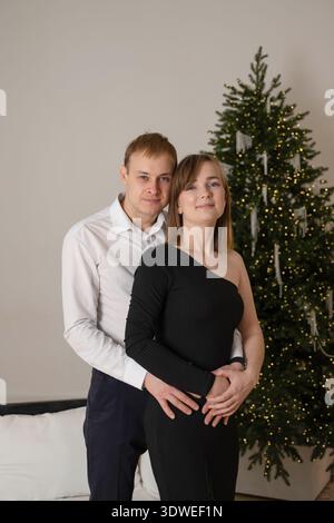 Una coppia gioiosa abbraccia amorevolmente di fronte a un albero di Natale splendidamente decorato, celebrando le festività natalizie e catturando il calore e la gioia Foto Stock