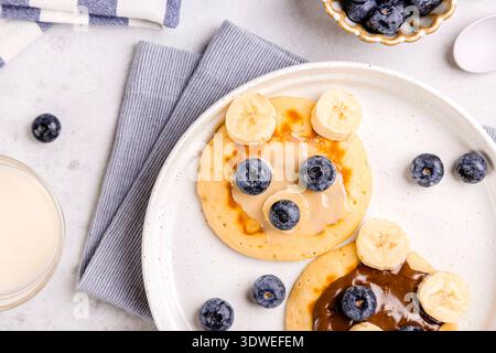 Una deliziosa colazione con soffici pancake conditi con mirtilli freschi e fette di banana. La configurazione invitante promette un inizio delizioso Foto Stock