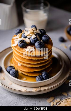 Deliziosa colazione con una pila di soffici pancake ricoperti di mirtilli freschi e mandorle a scaglie. Le frittelle sono ricoperte di sciroppo, aggiungere Foto Stock