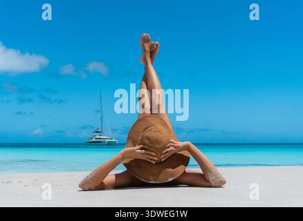 Donna in un cappello che si rilassa sulle sabbie incontaminate di Anse Georgette, Praslin. L'oceano turchese e il cielo azzurro creano un perfetto paradiso tropicale Foto Stock