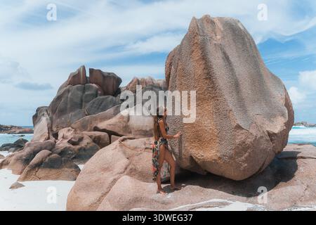Un viaggiatore ammira gli splendidi massi sulla pittoresca spiaggia di Anse Cocos, situata sull'isola di la Digue. Le formazioni rocciose uniche creano un ambiente sereno Foto Stock