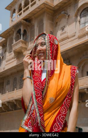 Donna in vivace abbigliamento tradizionale si erge graziosamente di fronte a uno storico tempio indiano, mostrando il ricco patrimonio culturale e l'architettura di Foto Stock