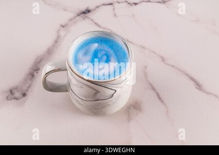 Un bellissimo latte matcha blu servito in un'elegante tazza di marmo, posto su una superficie liscia di marmo. Il vivace colore blu e lo sfondo elegante creano un Foto Stock