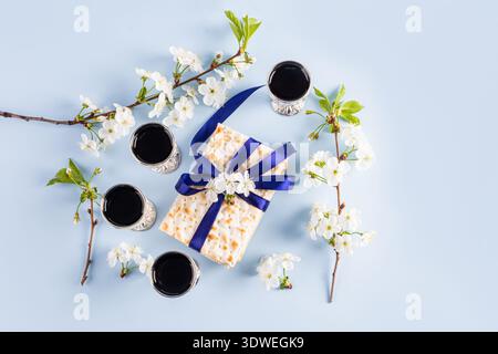 Un bellissimo allestimento di Pesach caratterizzato da una tradizionale matzah legata a un nastro blu, circondata da quattro tazze di vino e rami fioriti, che incarnano la loro bellezza Foto Stock